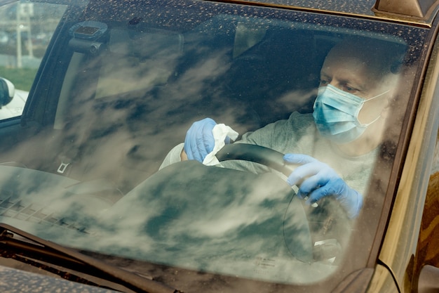 Un uomo in guanti e maschera pulisce il volante con una salvietta disinfettante