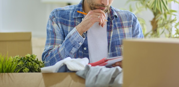 Un uomo in movimento seduto sul pavimento in un appartamento vuoto tra le scatole che controlla l'elenco delle cose