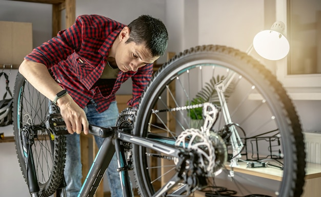 Un uomo in officina sta smontando la sua bicicletta e la ripara. Concetto di manutenzione e preparazione per la nuova stagione