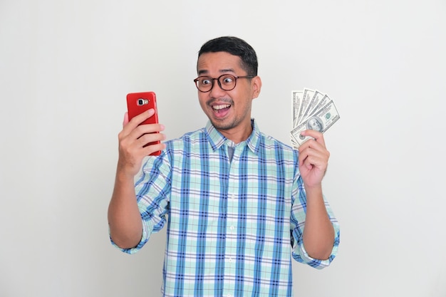 Un uomo in possesso di denaro in dollari USA che mostra un'espressione sorpresa mentre guarda al suo handphone