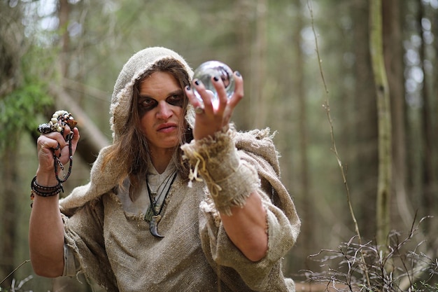 Un uomo in tonaca trascorre un rituale in una foresta oscura con una sfera di cristallo e un libro