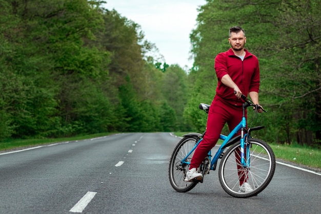 Un uomo in tuta sta accanto a una bicicletta su una strada nella foresta. Il concetto di uno stile di vita sano, allenamento cardio. Copyspace.