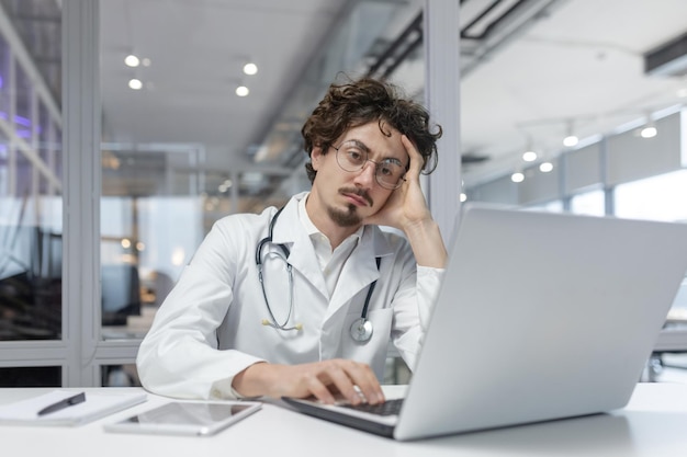 Un uomo in un cappotto medico bianco con uno stetoscopio si siede davanti a un computer portatile in un medico