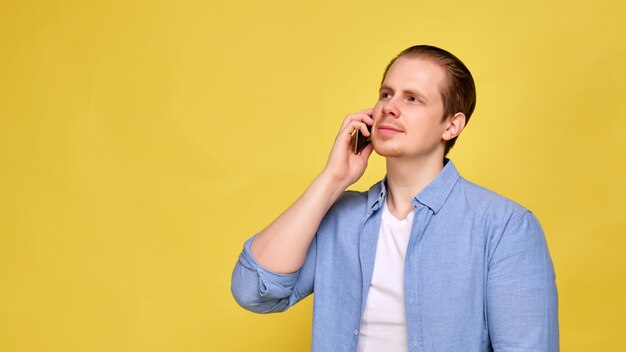 Un uomo in una camicia blu su uno sfondo giallo sta chiamando il suo smartphone.