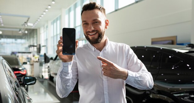 Un uomo in una concessionaria di automobili mostra lo schermo di uno smartphone con un sorriso