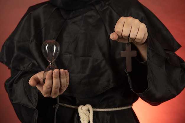 Un uomo in una tonaca monastica tiene una clessidra e un crocifisso nelle sue mani
