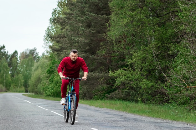 Un uomo in una tuta da ginnastica su una bicicletta cavalca su una strada nella foresta. Il concetto di uno stile di vita sano, allenamento cardio. Copyspace.