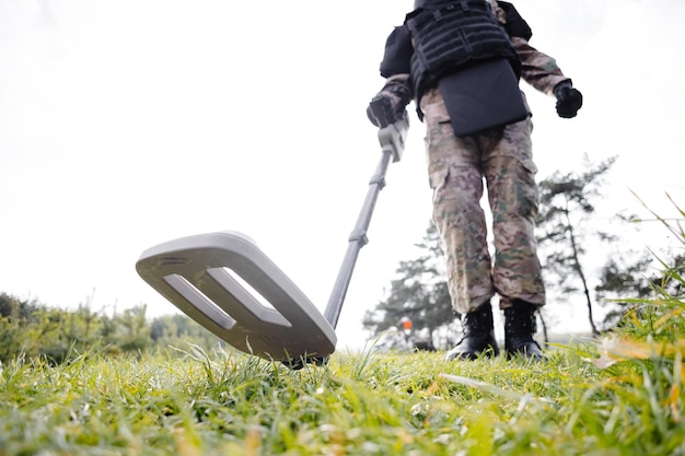 Un uomo in uniforme militare e giubbotto antiproiettile lavora nella foresta con un metal detector Un dragamine esegue lavori di sminamento del territorio