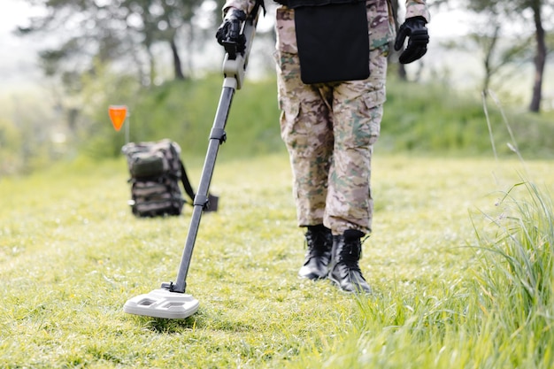 Un uomo in uniforme militare e giubbotto antiproiettile lavora nella foresta con un metal detector