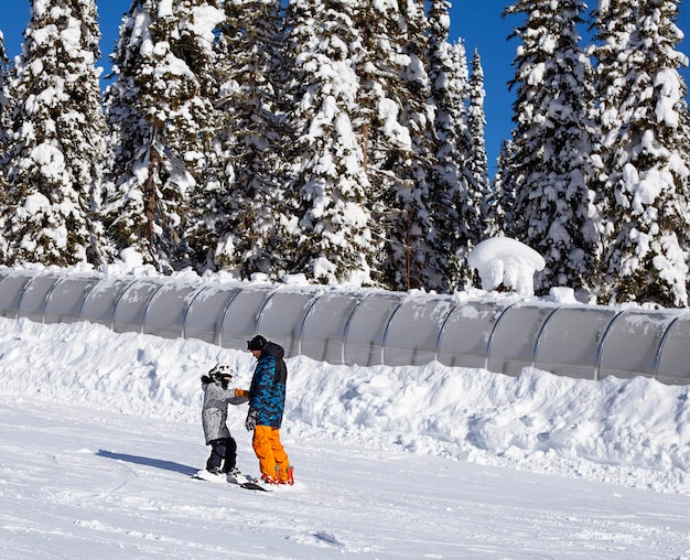 un uomo insegna a un bambino a fare snowboard su una pista da sci