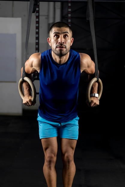 Un uomo latino in abbigliamento sportivo che fa esercizi ginnici su alcuni anelli in una palestra