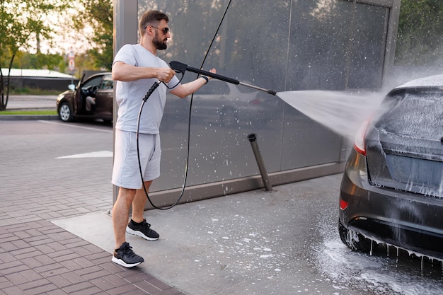 Un uomo lava la schiuma con un cannone ad acqua in un lavaggio auto Un'auto in un lavaggio auto self-service