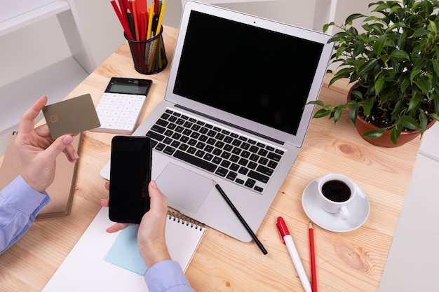 Un uomo lavora con laptop, calcolatrice, penne, matite, carta, telefono e una pianta sul suo desktop in ufficio