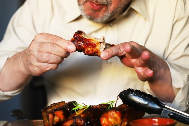 Un uomo mangia le costolette di maiale al forno con le mani. L'uomo sta mangiando carne. Cibo spazzatura. Carne fritta, conceragen.