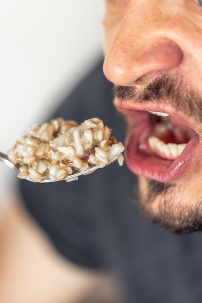 Un uomo mangia porridge con frutta e la bocca dell'uomo è aperta