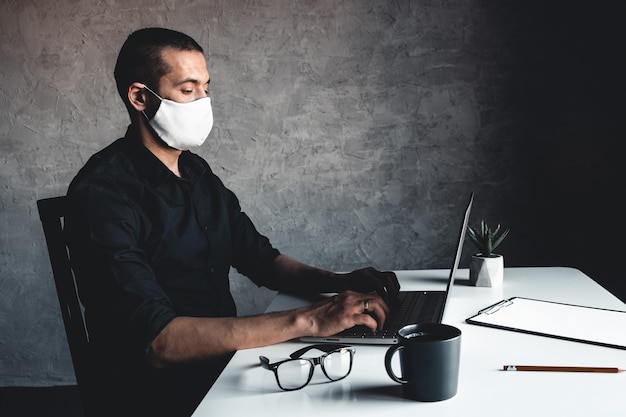Un uomo mascherato lavora al computer. Pandemia, coronavirus, epidemia