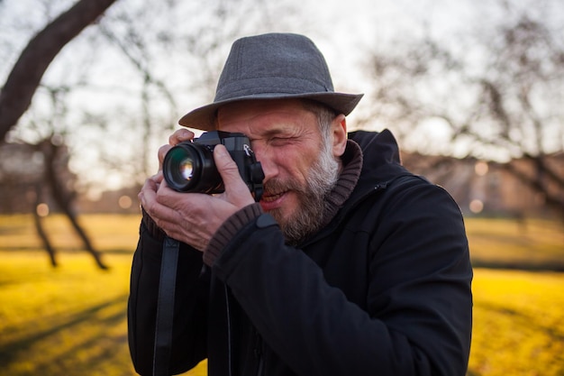 Un uomo maturo con un cappello scatta foto con una fotocamera mirrorless per strada Hobby della fotografia Nuove tendenze nella tecnica fotografica