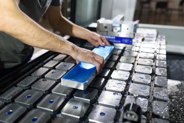 un uomo mette un pezzo di alluminio su una macchina cnc e prepara una macchina per la lavorazione.