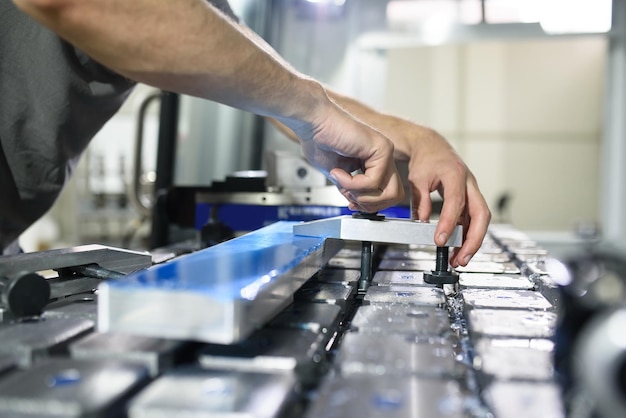 un uomo mette un pezzo di alluminio su una macchina cnc e prepara una macchina per la lavorazione.