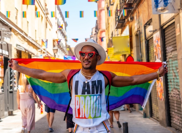 Un uomo nero gay che cammina indossando occhiali da sole alla festa dell'orgoglio con una bandiera LGBT