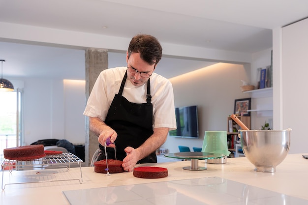 Un uomo panettiere che cucina una torta di velluto rosso a casa che taglia la torta al forno con una lira