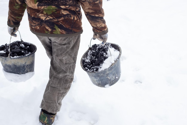 Un uomo porta due secchi di carbone per riscaldare una casa in un villaggio in una giornata invernale nevosa