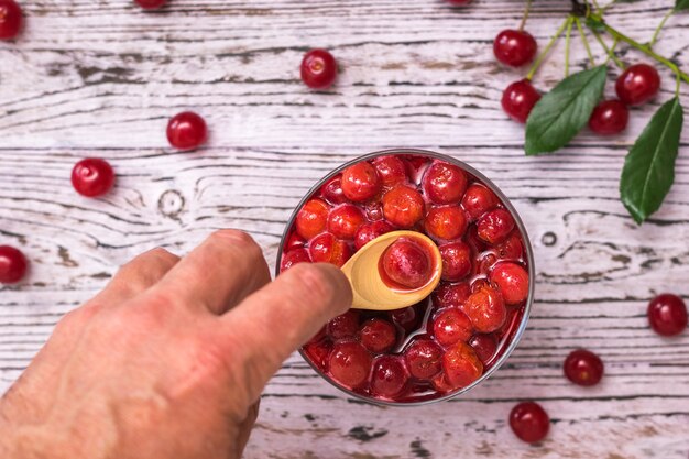 Un uomo prende una bacca di ciliegia di un cucchiaio di legno da una ciotola di marmellata