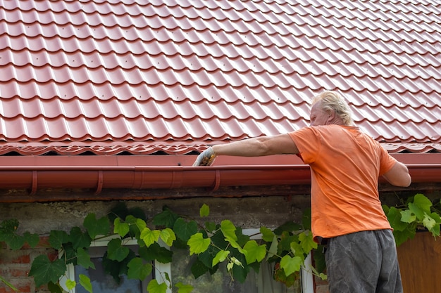 Un uomo pulisce detriti e foglie dal sistema di grondaie sul tetto della sua casa