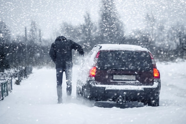 Un uomo pulisce un'auto dalla neve parcheggiata sul lato di una strada invernale