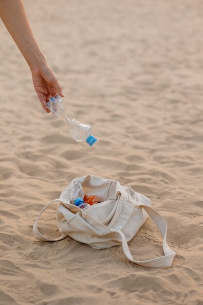 Un uomo raccoglie bottiglie di plastica e spazzatura sulla spiaggia in un luogo pubblico eco friendly e premuroso