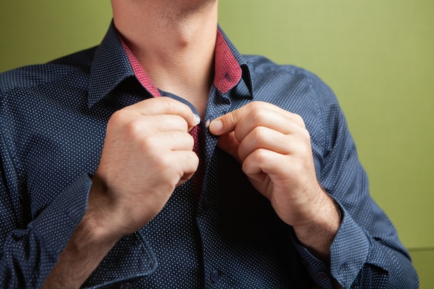 Un uomo raddrizza il bottone del colletto della sua camicia su uno sfondo verde