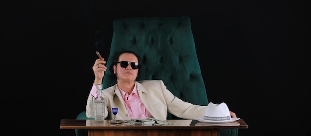 un uomo ricco in abito bianco si siede su una sedia sullo sfondo di uno studio nero