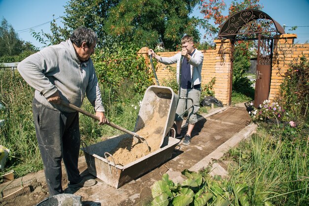 Un uomo scarica la sabbia in una miscela di cemento per versare un percorso del giardino, lavori di costruzione su un appezzamento di giardino