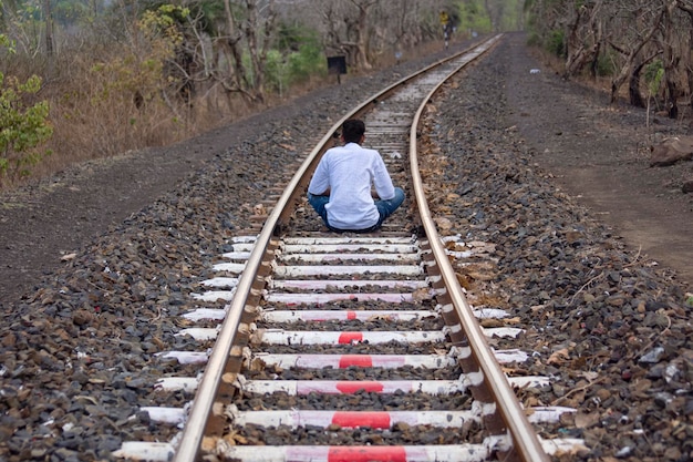 Un uomo seduto sul binario ferroviario in posa meditando al villaggio di montagna Kalakund Madhya Pradesh