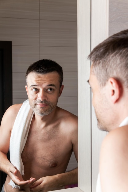 Un uomo si guarda allo specchio del bagno al mattino con un asciugamano sulla spalla