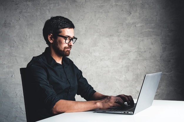 Un uomo si siede con un laptop in una camicia nera. Concetto di affari, lavoro. Routine d'ufficio. Sforzi di proprietà