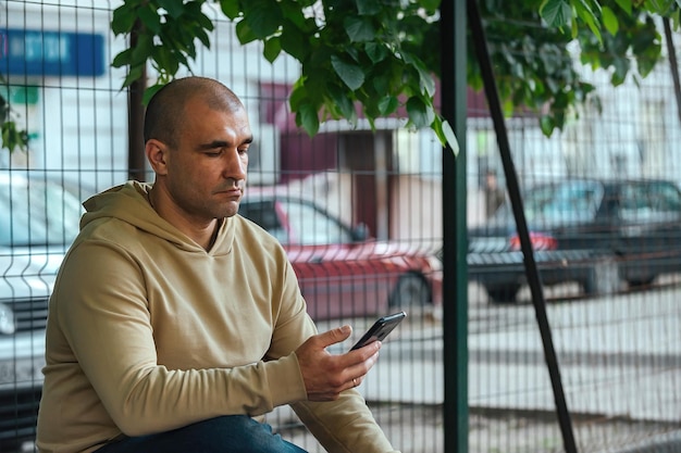 un uomo si siede su una panchina nel parco per una passeggiata e guarda attraverso il suo telefono