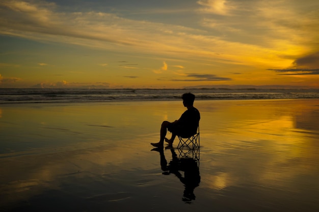 Un uomo si siede su una sedia sulla spiaggia al tramonto.