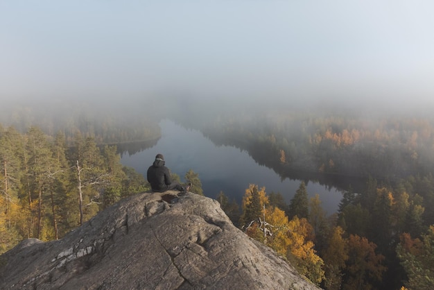 Un uomo si siede sulla cima di una vista nebbiosa atmosferica di una montagna di granito