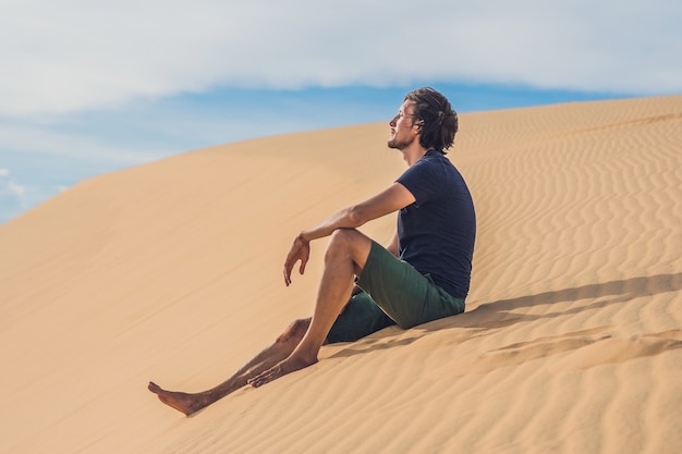 Un uomo si siede sulla sabbia nel deserto.