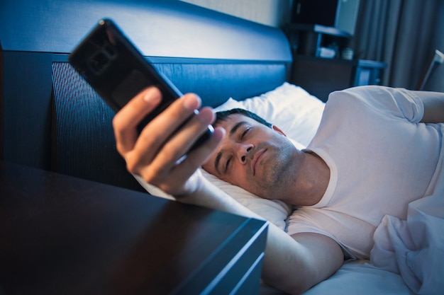 Un uomo si sveglia a letto e guarda il telefono, spegne la sveglia e guarda l'ora, naviga in Internet, legge messaggi, controlla i social network.