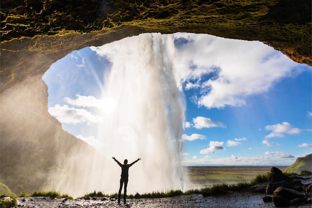 Un uomo si trova di fronte a una cascata con le braccia alzate in aria.