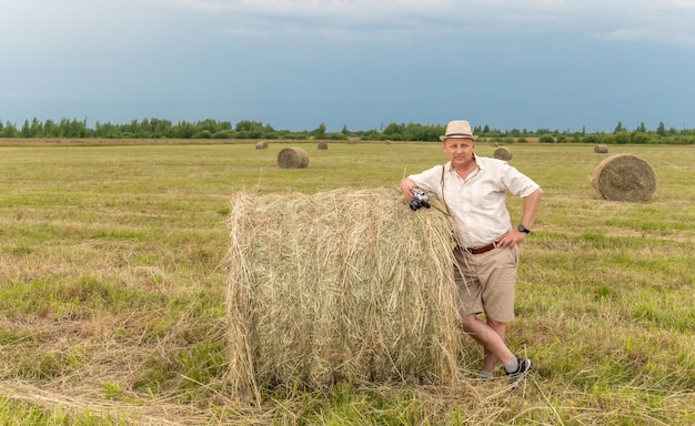 Un uomo si trova in un campo con una grossa balla di fieno.