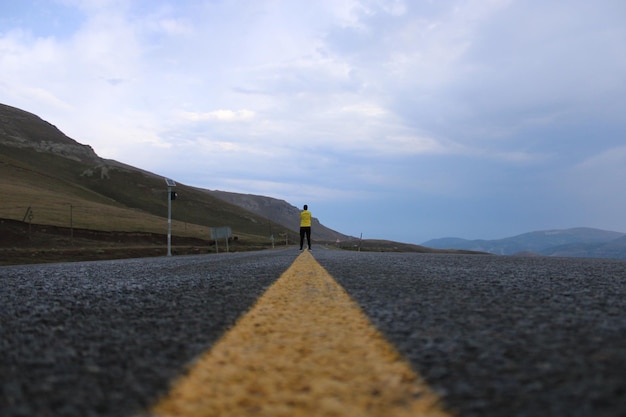 Un uomo si trova sulla strada di fronte a una montagna.