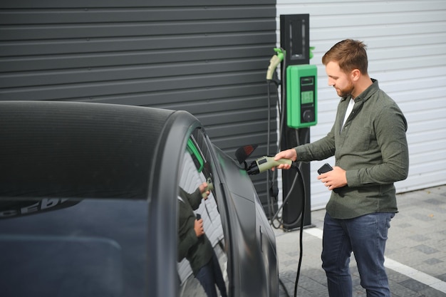 Un uomo si trova vicino a una stazione di ricarica e ricarica la sua auto elettrica