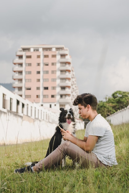 Un uomo siede in un campo con il suo cane e guarda il suo telefono.