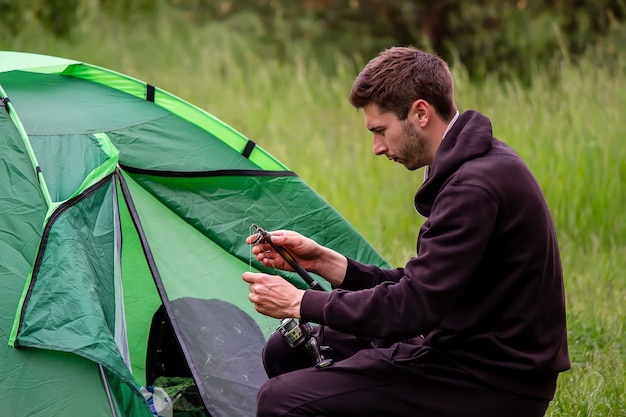 Un uomo siede vicino a una tenda turistica. Natura, svago, campeggio. Messa a fuoco selettiva