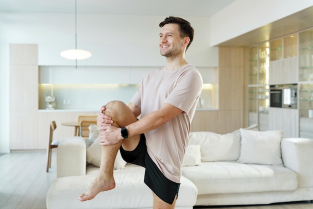 Un uomo soddisfatto esegue un allungamento di yoga in piedi bilanciandosi con grazia in un moderno salotto ben illuminato