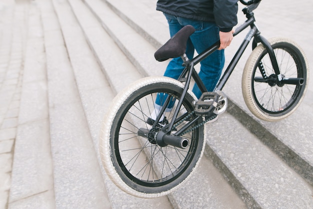 Un uomo solleva la bici BMX sulle scale verso l'alto. Un uomo con una bici BMX. Copyspace.