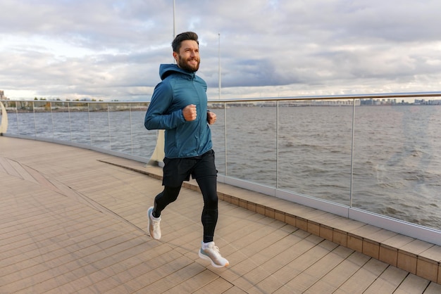 Un uomo sorridente che corre sul lungomare si gode un allenamento dinamico con lo sfondo panoramico della città